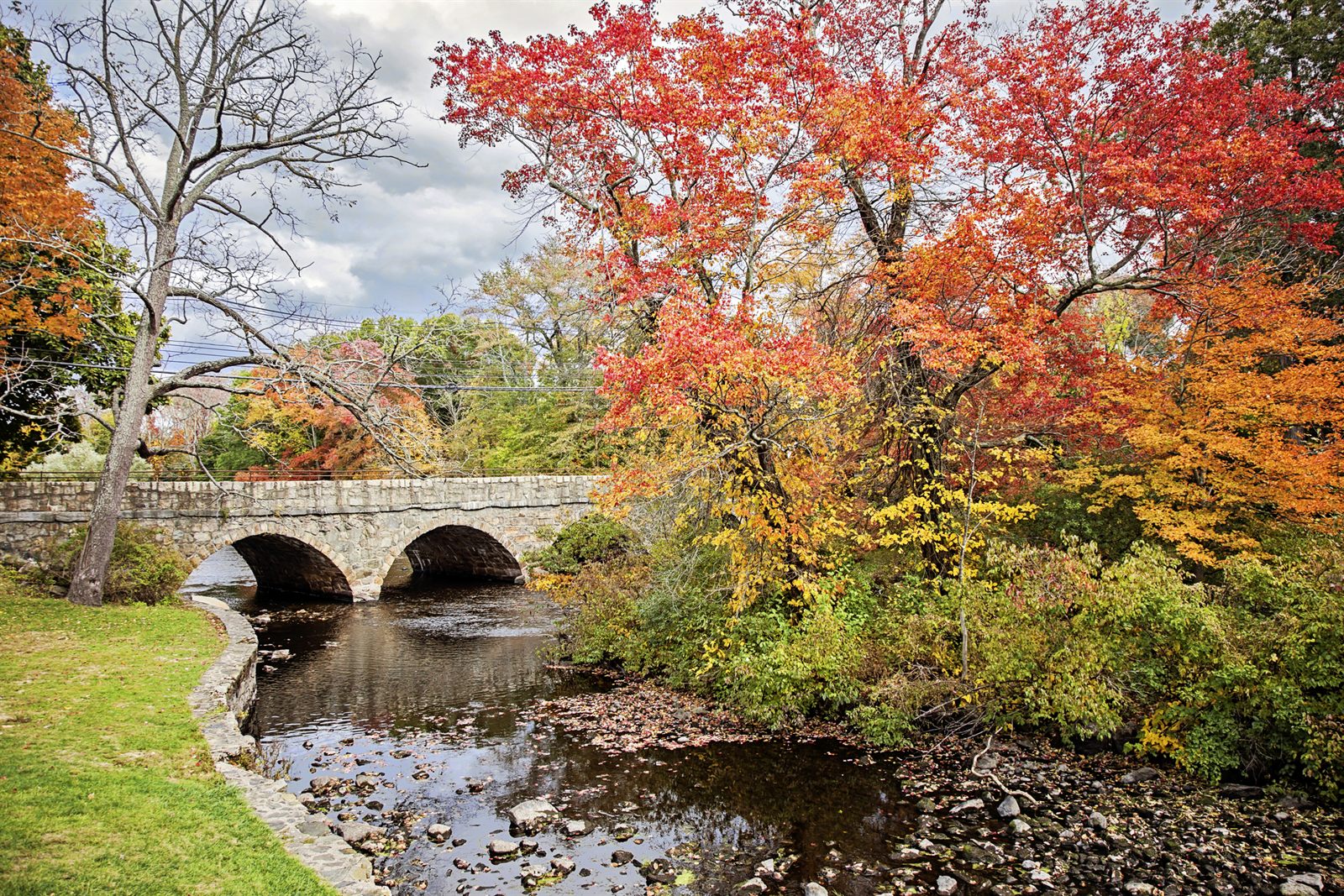 A stone arch bridge over a rocky stream among trees in red and orange fall color