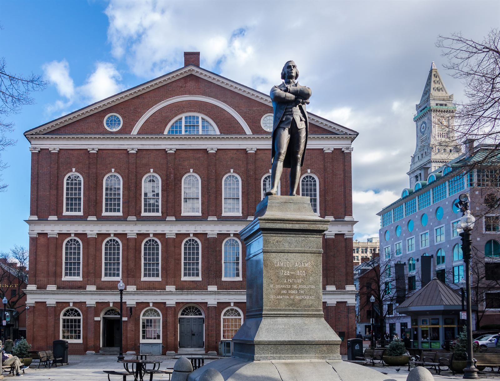 Faneuil Hall in Boston, a red brick hall with a cupola, behind a bronze statue of Samuel Adams