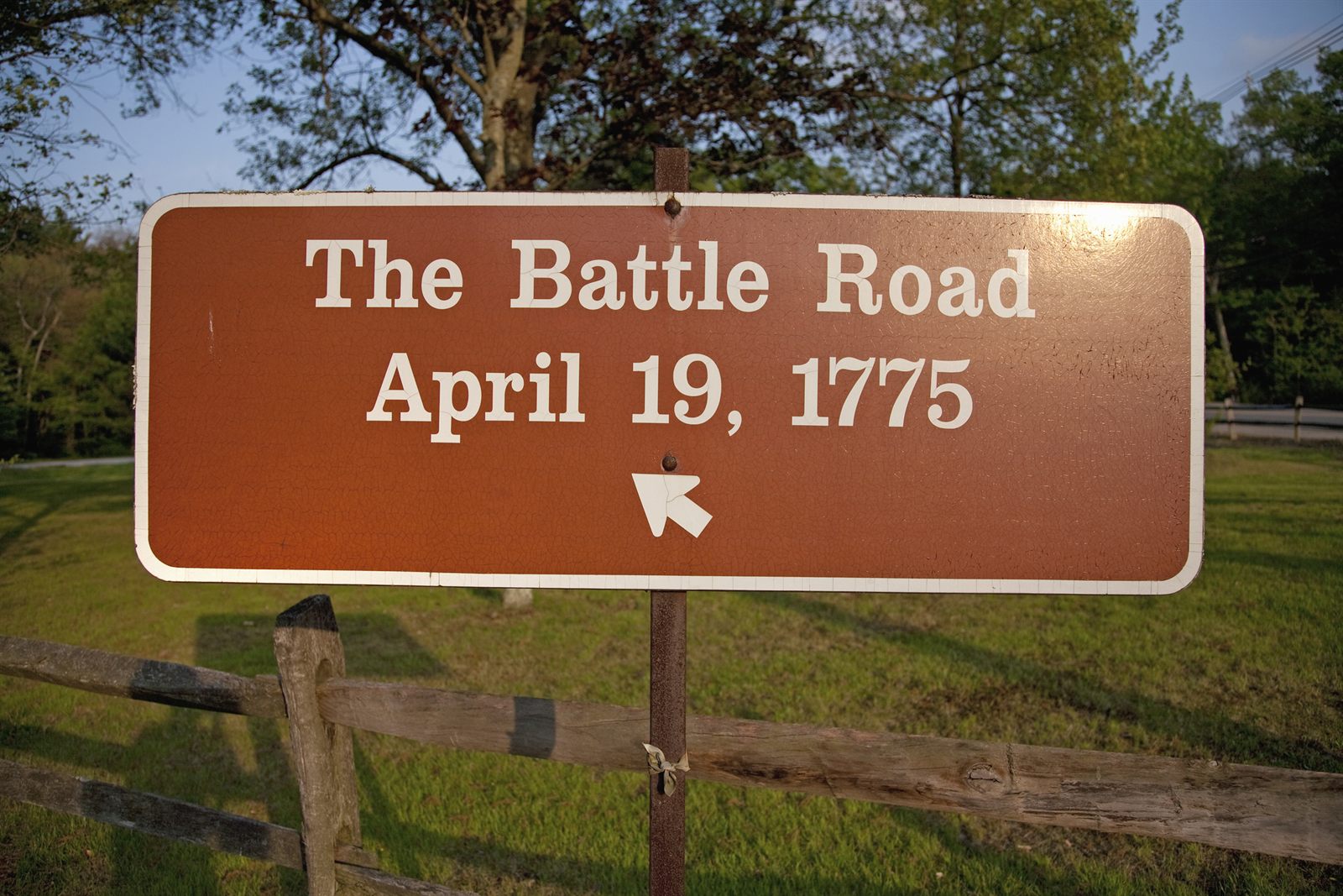A brown wooden sign reading The Battle Road, April 19, 1775, beside a grassy trail