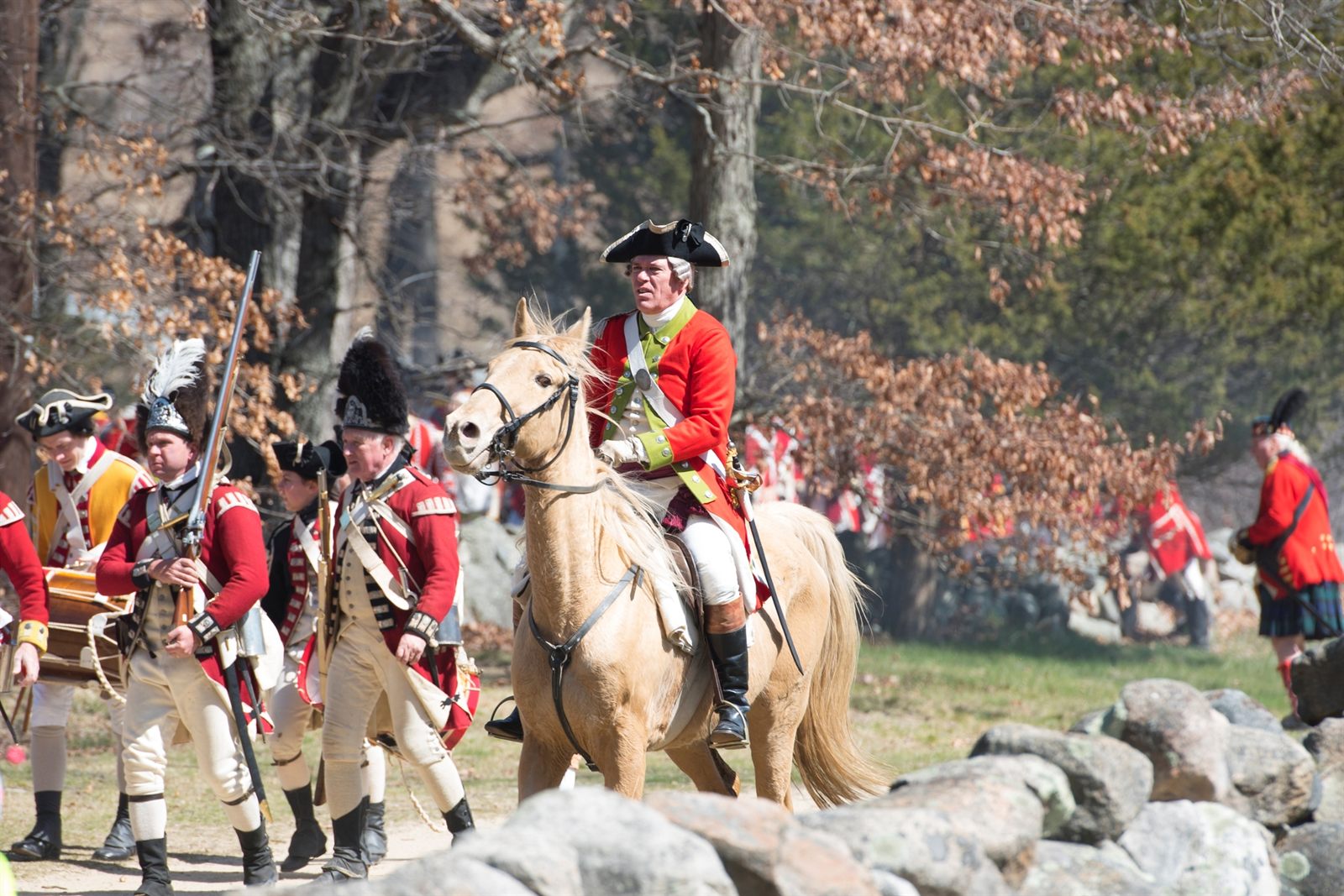 Reenactors in British redcoat uniforms marching behind an officer on horseback
