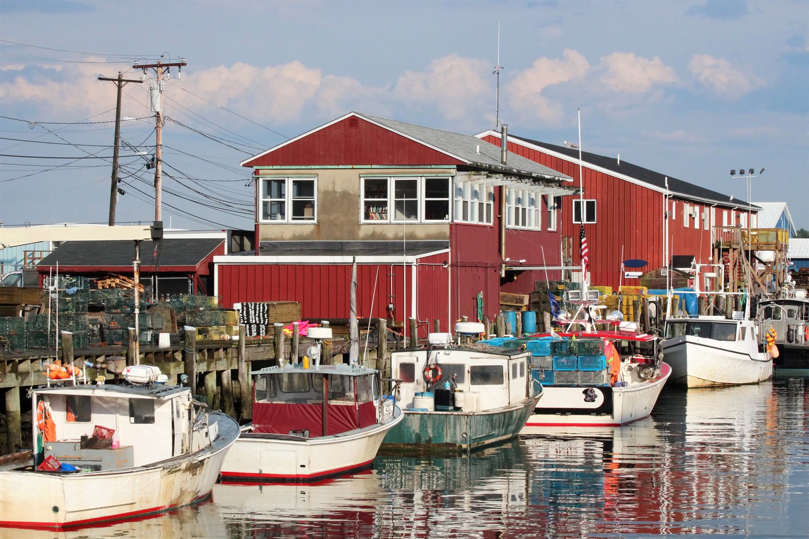 Lobster boats tied up below red wooden wharf buildings in a working New England harbor
